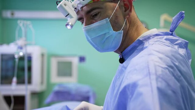 Side view of a surgeon in mask, headlight and colorful cap. Close up portrait of a professional focused on operation.