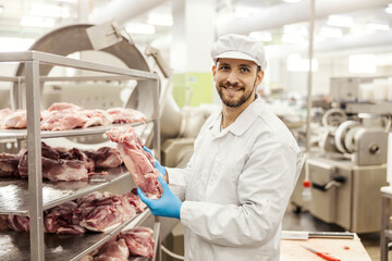 A meat factory worker is holding piece of raw meat and smiling at the camera. - Powered by Adobe