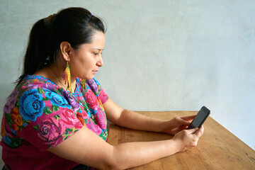 Guatemalan woman in traditional huipil dress working with laptop and smartphone