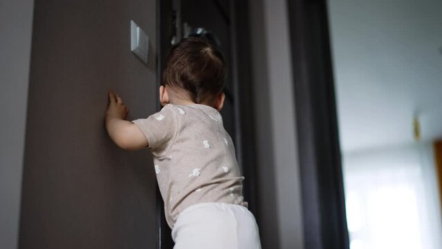 Rear view of a toddler standing at the door. Kid opens the door to a dark room looking for something. Low angle view.