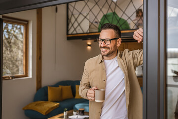 Fototapeta premium One adult man stand in at door of tiny house happy smile hold cup