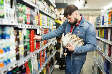 Stylish young glad guy in denim jacket choosing beers during shopping in food store