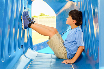 Young preteen boy sitting inside playground equipment looking at his sneakers on the wall in front of him