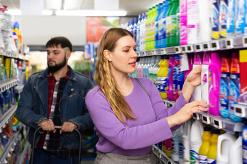 People making purchases in household chemistry store, woman choosing detergent, man on background