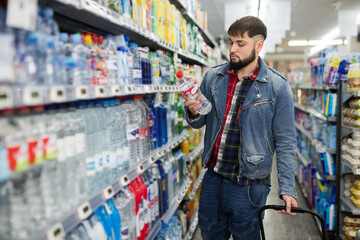 Stylish bearded man shopping in food store, choosing water in bottles.