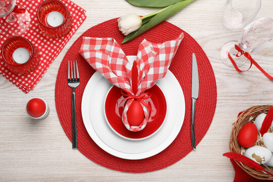 Festive table setting with bunny ears made of red egg and napkin, flat lay Easter celebration - Powered by Adobe