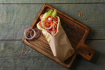 Delicious pita wrap with vegetables and meat on dark wooden table, top view