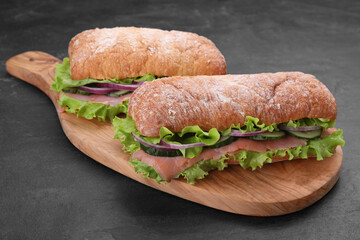 Delicious sandwiches with fresh vegetables and salmon on black table