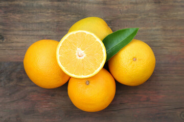 Many ripe oranges and green leaf on wooden table, flat lay