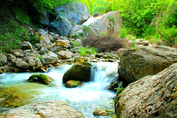 Fresh scenery with lively green nature and gargantuan grey and brown rocks surrounding a glowing and translucent stream of pure mountainous waters from the Ambro river on a perfect summer day