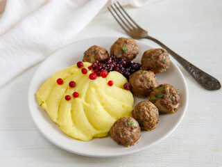 Swedish Kottbullar meatball with mashed boiled potatoes and cowberry sauce on white plate on white background