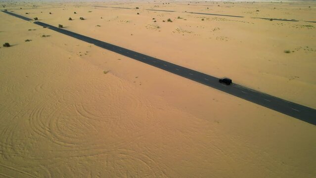 Aerial tracking shot of a black SUV traveling through the desert in Dubai, UAE