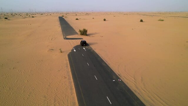 Aerial tracking shot of a black SUV traveling through the desert in Dubai, UAE
