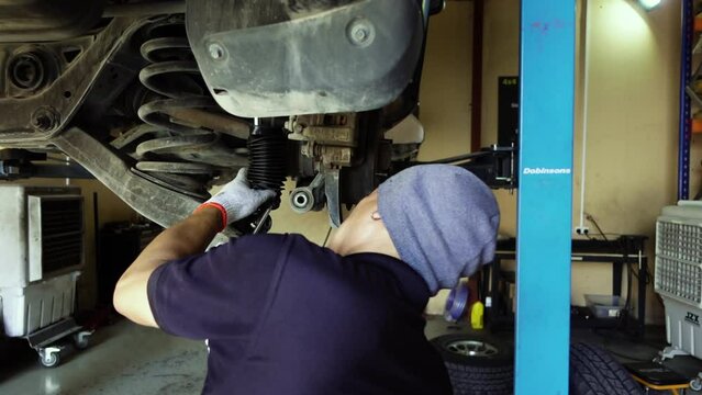Slow motion shot of a mechanic putting a new suspension on an SUV in a garage