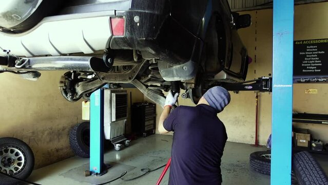 Slow motion dolly shot of a mechanic putting a new drive shaft on an SUV