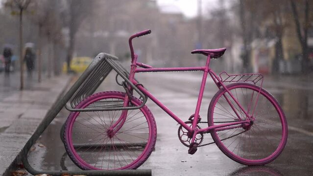 Pink singlespeed bicycle locked up against bike rack on wet cold day in Bulgaria
