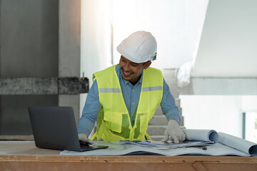 asian male engineer working with drawings inspection on laptop on construction site at work desk in...
