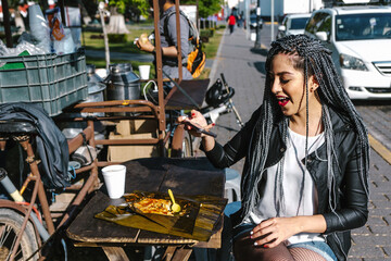 Fototapeta premium young latin woman with braids hair eating mexican tamales street food on park in Mexico city, hispanic people