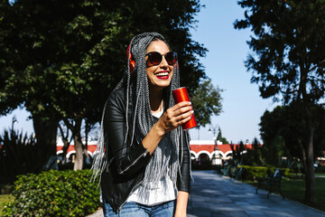 Young latin woman with braids hair holding beverage drink soda can on the street in Mexico,...