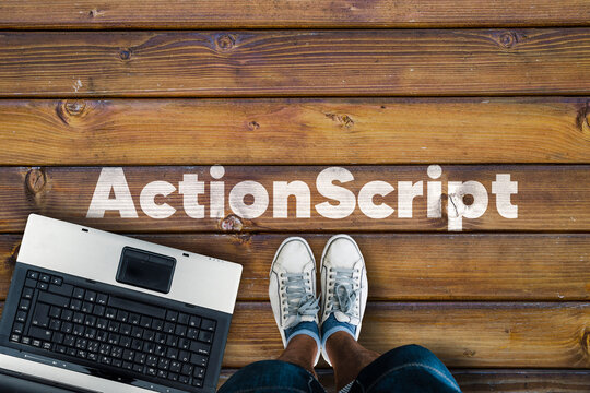 Legs in sneakers standing next to laptop and  wordActionScript on wooden floor. ActionScript programming language. 
