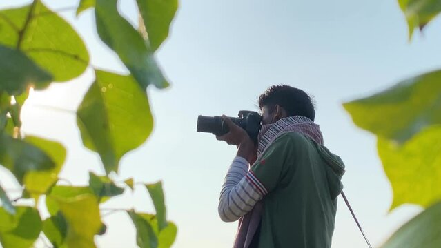 Man raises camera to take pictures and reviews photo, framed by leaves