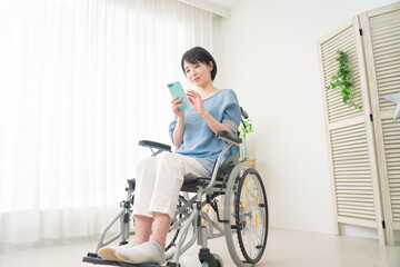 Naklejka premium リビングでスマホを使う車椅子に乗った女性