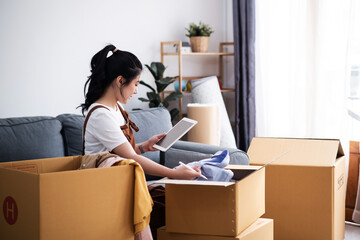 Fototapeta na wymiar New house, asian woman check list of stuff in the box while feeling proud and excited about buying a house with a mortgage loan. Young asian woman first time buyers unpacking in dream home, apartment