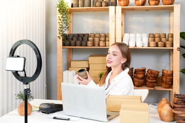 Review handmade wooden vase and coaster while recording live video with mobile and ring light by Caucasian young entrepreneur girl