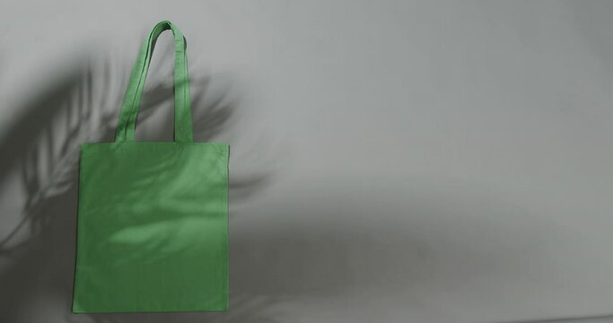 Leaf shadow moving over green bag on grey background, copy space, slow motion
