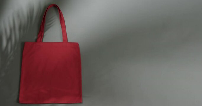 Leaf shadow moving over red bag on grey background, copy space, slow motion