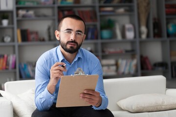Male psychoanalyst sitting on sofa with clipboard.