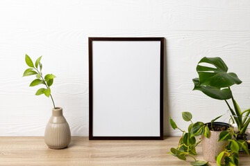 Black empty frame with copy space and plants in pots on table against white wall