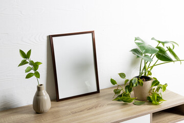 Black empty frame with copy space and plants in pots on table against white wall