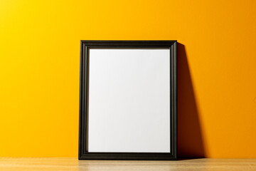 Black empty frame with copy space on table against yellow wall