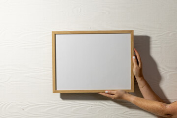 Hands holding wood empty frame with copy space against white wall