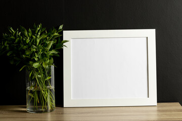 White empty frame with copy space and plant in pot against black wall