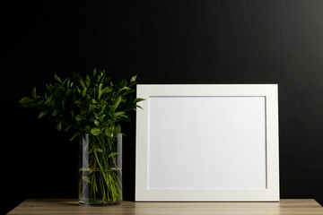 White empty frame with copy space and plant in pot against black wall