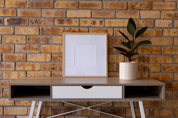 Wood empty frame with copy space and plant in pot on desk against brick wall