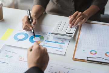 Team of business people is calculating with a calculator and discussing to record company financial growth statistics using graphs. The chart is a reference for auditing and analyzing the summary.