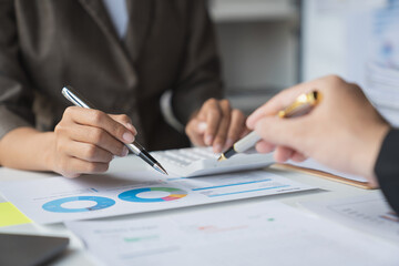 Team of business people is calculating with a calculator and discussing to record company financial growth statistics using graphs. The chart is a reference for auditing and analyzing the summary.