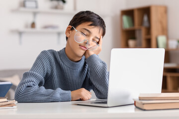 Little boy in eyeglasses sleeping near laptop at home