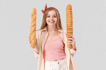 Young woman with fresh baguettes on grey background