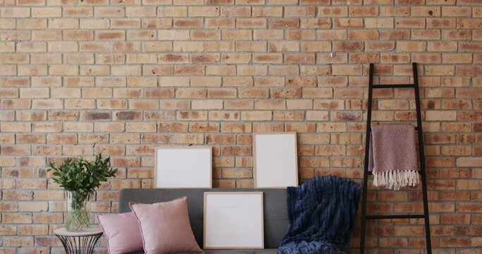 Three wooden frames, plant and sofa with copy space on brick wall