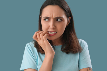 Young woman biting nails on blue background, closeup