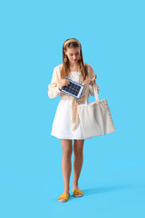 Pretty young woman with portable solar panel on blue background