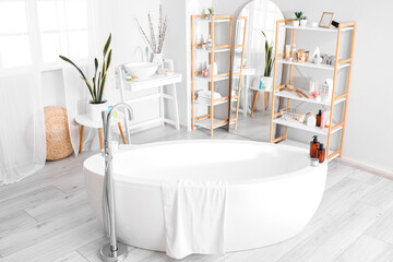 Interior of bathroom with bathtub, mirror and shelving units