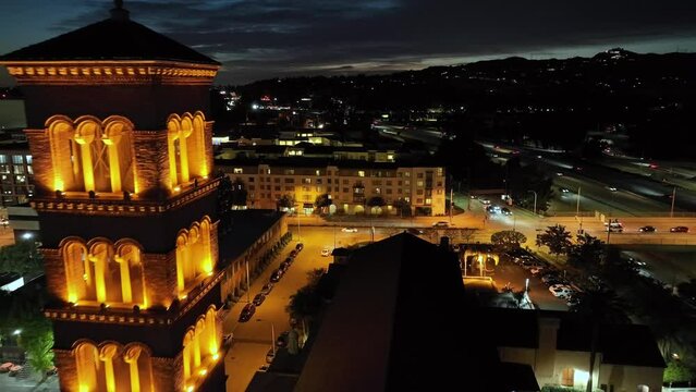 Aerial view passing illuminated clock and church bell tower overlooking Pasadena blue hour city landscape, Los Angeles