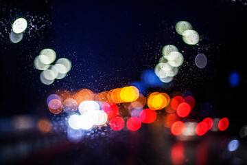 abstract background of blurred multicolored light from headlights on a wet windshield of a car in...