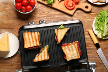 Delicious sandwiches with modern electric grill on wooden table