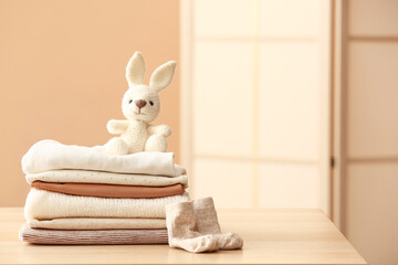 Stack of baby clothes, socks and toy bunny on table in room